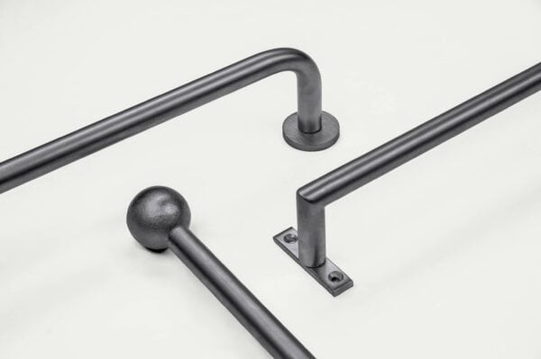 Three black metal handrails on a white surface, each with different attachment bases: round, square, and spherical ends.