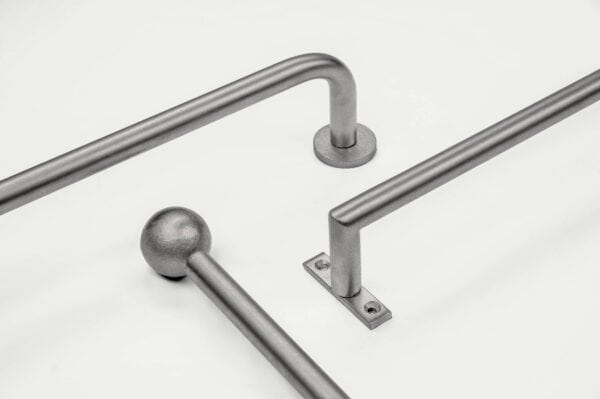 Three silver metallic handrails on a light surface, featuring different shapes and mounting bases.