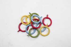 A pile of colorful Standard Curtain Rings in red, yellow, blue, and green lies on a white surface.