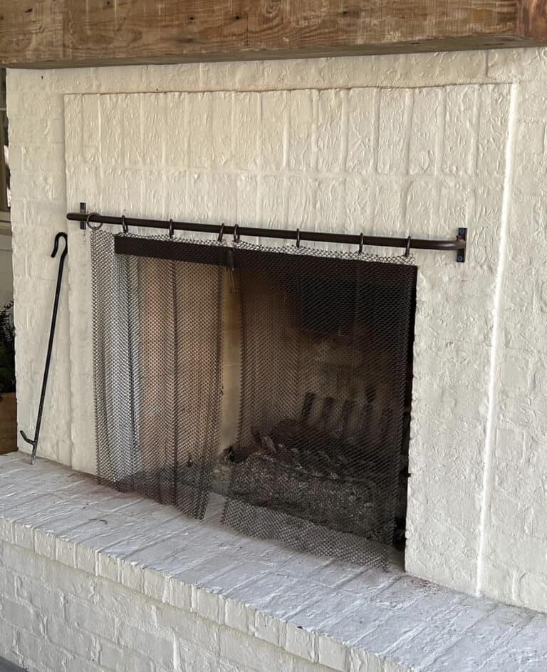 A white brick fireplace with a metal mesh screen and a poker tool leaning against it.