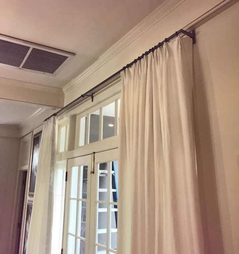 White curtains hang from a rod above a glass-paneled door in a room with beige walls and white crown molding.