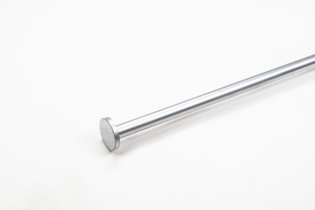 A long, smooth, metallic rod with a flat circular end is positioned diagonally on a plain white background.