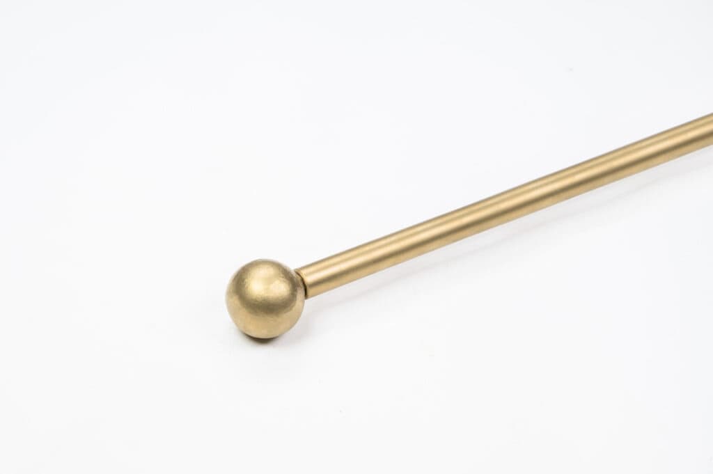 A brass rod with a spherical end is placed diagonally against a plain white background.