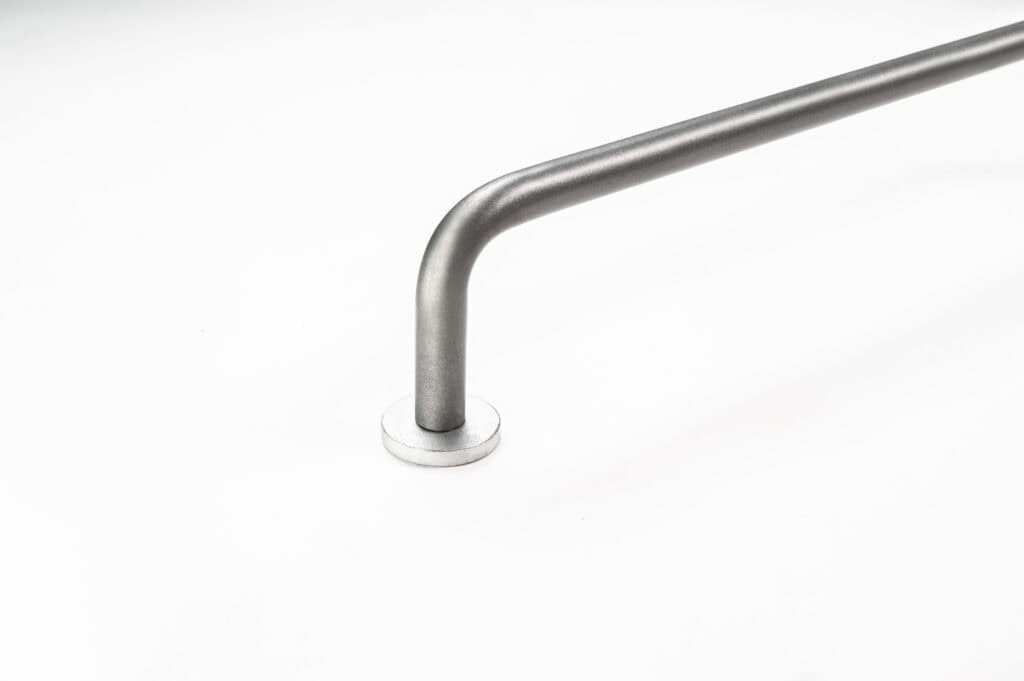 A close-up of a metal handrail attached to a white wall, showing a right-angle bend and a circular mounting plate.
