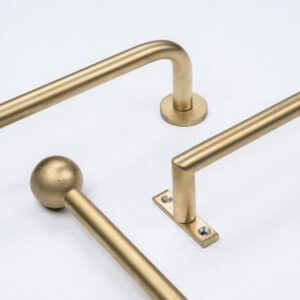 Three gold-colored metal handles with varied ends, resembling elegant curtain rods, placed on a white surface.