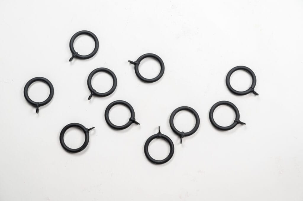 Ten black metal rings with small tabs, crafted with care, are scattered on a plain white surface.